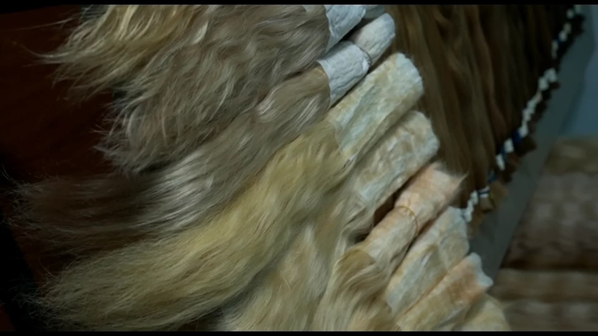 A wall of muslin-wrapped hair bundles hanging in shade order, from blonde to deep brown