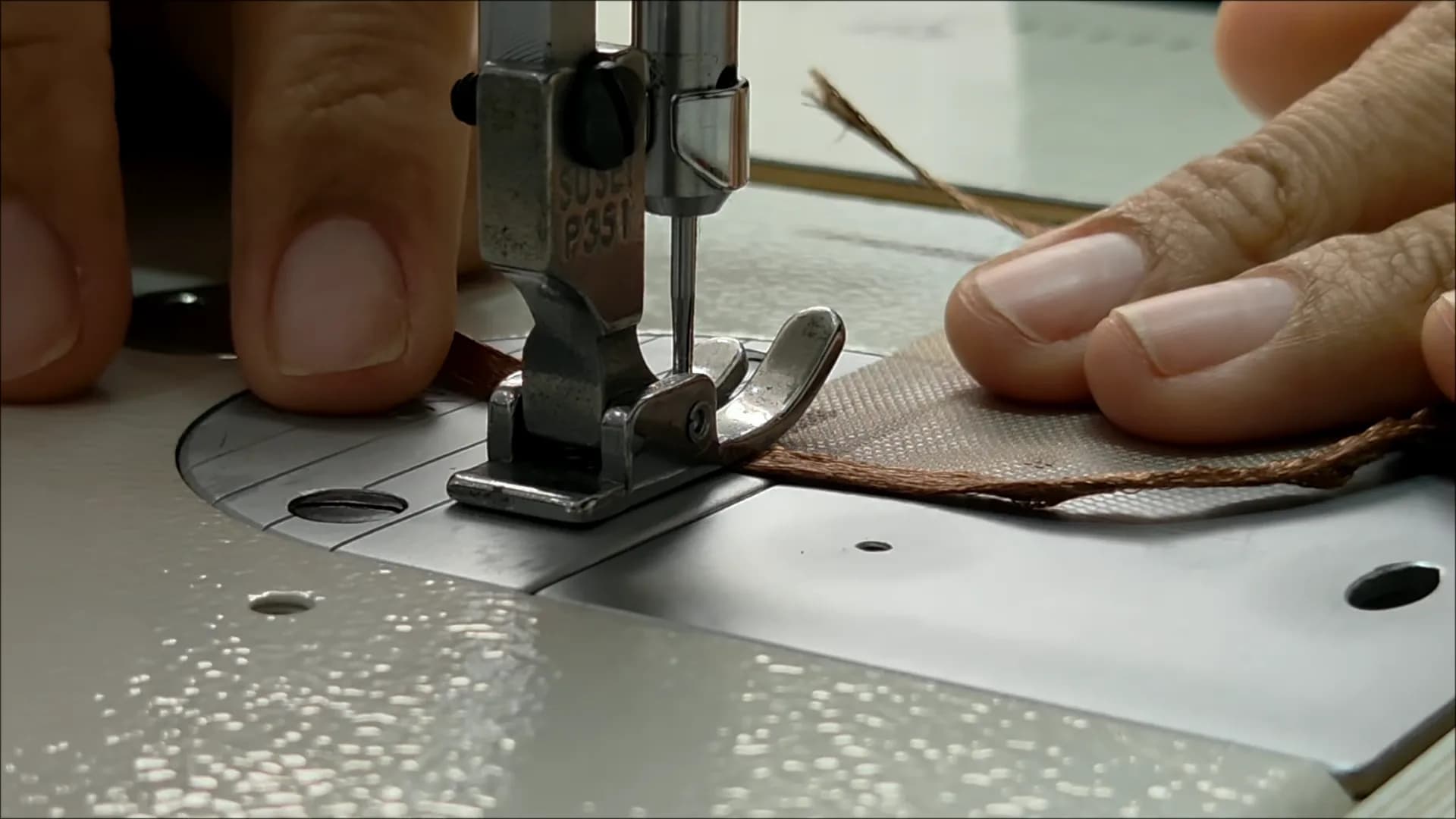 An artisan's fingers guiding a hair weft under the needle of a sewing machine
